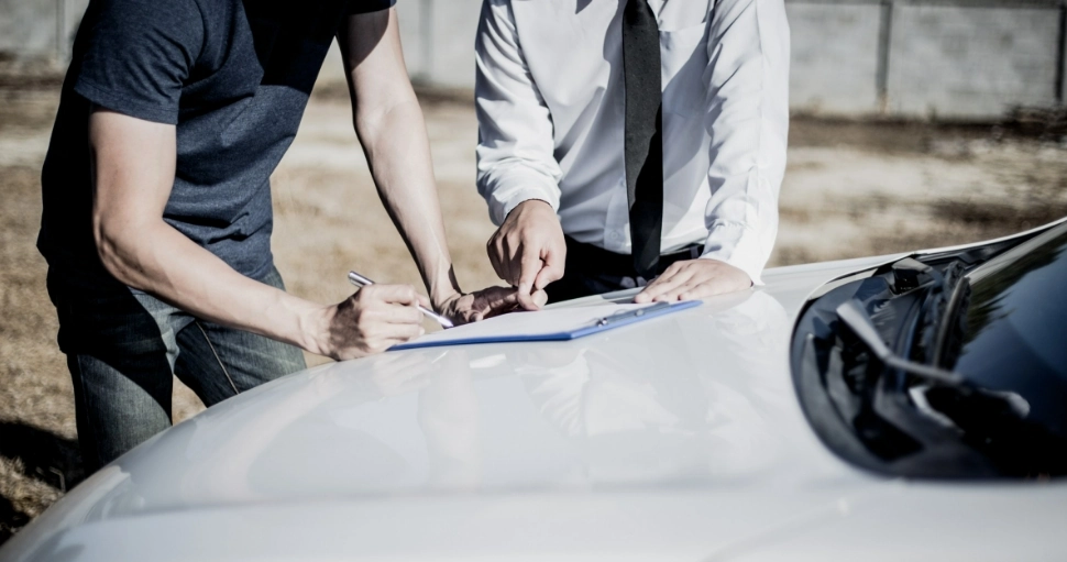 Dwie osoby uzupełniające dokumenty na masce samochodu